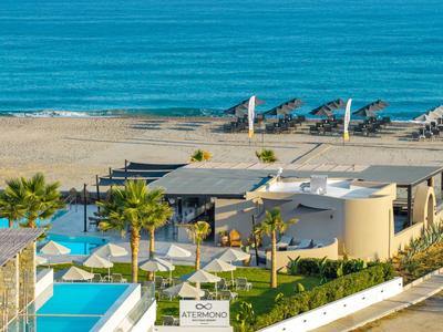 Modern hotel area with pool, green garden, and view of the sea.