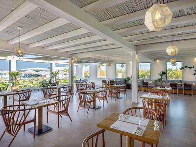 Bright restaurant with wooden chairs and tables, large windows overlooking outdoor area.
