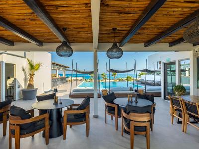 Open hotel outdoor area with tables, chairs, pool, and sea view.