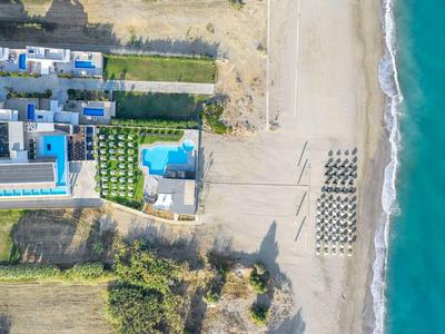 Aerial view of a hotel with pool next to a beach with umbrellas and blue sea.