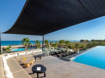 Modern outdoor pool with lounge areas, sea view, and shade sails under clear sky.