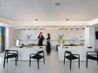 Bright hotel lobby with modern reception, seating, and two staff members behind the counter.
