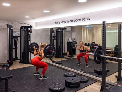 Woman exercises with barbell in hotel gym with mirrored wall.