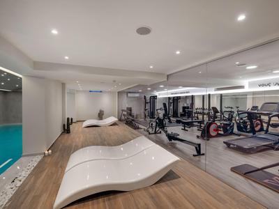 Modern fitness room with indoor pool, relaxing loungers, and various exercise equipment.