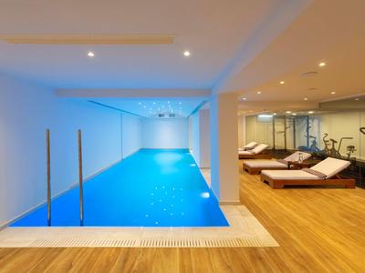Piscine intérieure dans un espace bien-être moderne avec des transats et un sol en bois.