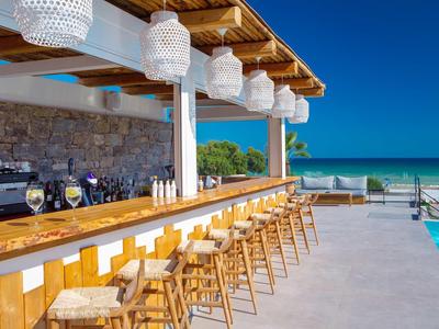 Offene Strandbar mit Holztheke, Hockern, weißen Lampen und Blick auf türkisblaues Meer.