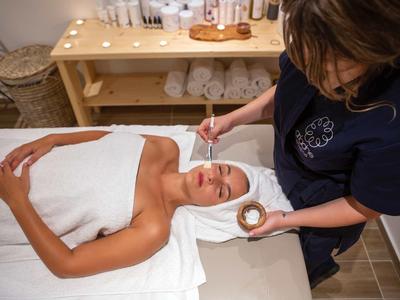 Femme recevant un soin du visage dans un spa avec des serviettes dans une ambiance calme.