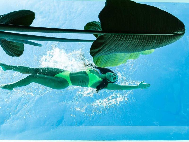Femme nageant sous l'eau dans une piscine avec de grandes feuilles au-dessus