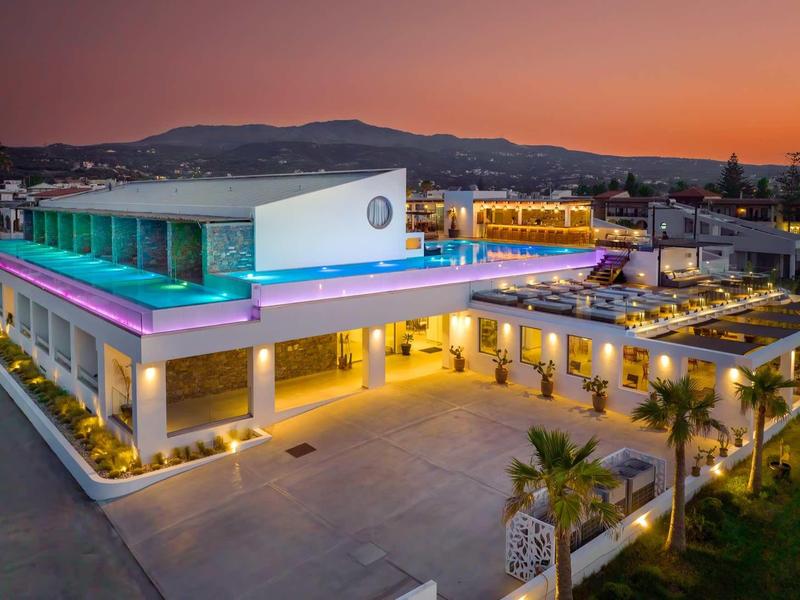 Hôtel moderne avec piscines éclairées et palmiers au coucher du soleil.