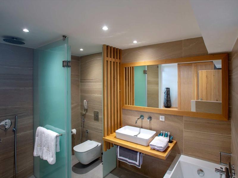 Salle de bain d'hôtel moderne avec accents en bois, douche en verre, lavabo, toilettes et serviettes.