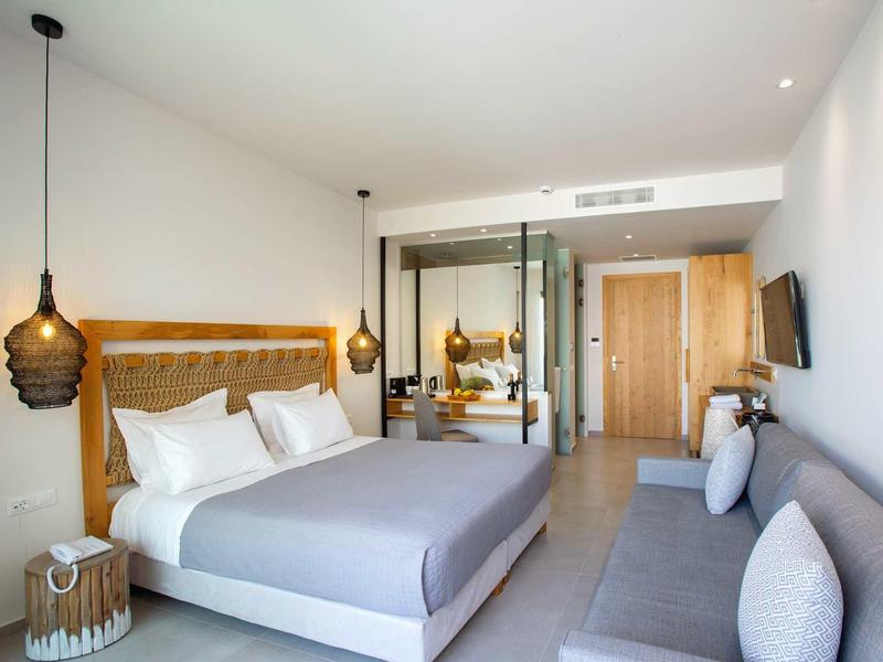 Chambre d'hôtel moderne avec grand lit, canapé et éclairage chaleureux.