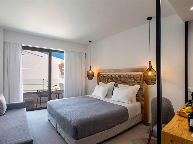 Chambre d'hôtel moderne avec lit double, canapé, balcon et éclairage élégant.