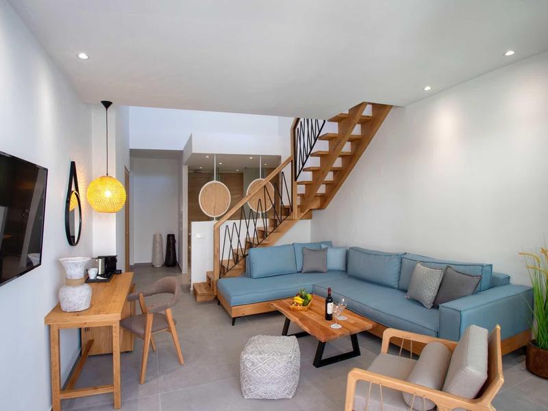 Salon moderne avec canapé d'angle bleu, meubles en bois et escalier en arrière-plan.