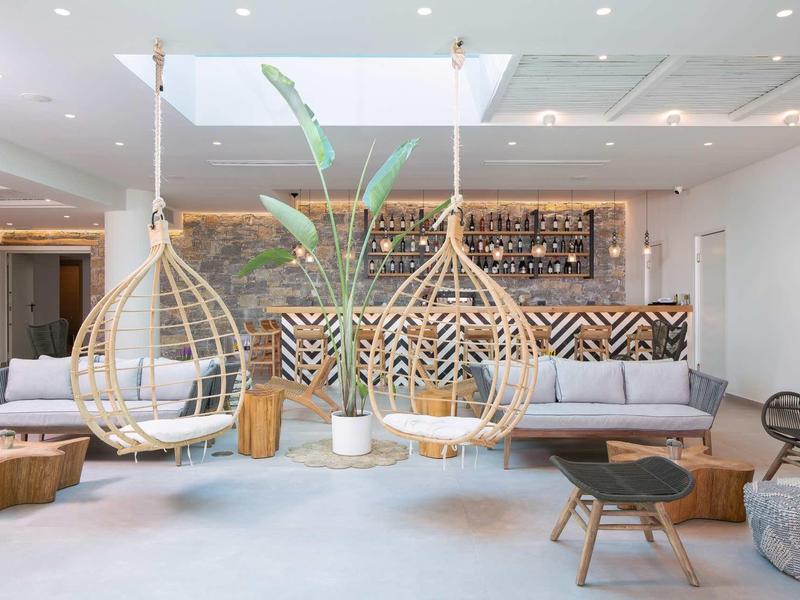 Chambre d'hôtel moderne avec fauteuils suspendus en rotin, canapé et meubles en bois dans un cadre lumineux.