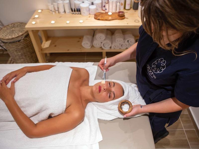 Femme recevant un soin du visage dans un spa avec des serviettes dans une ambiance calme.