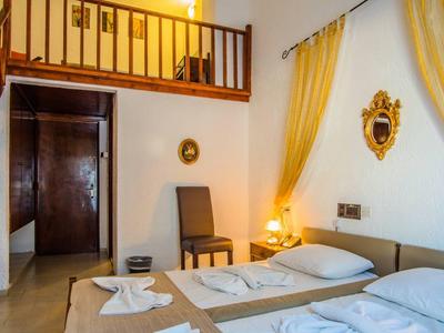 Cozy hotel room with two single beds, chair, balcony, and yellow curtains.