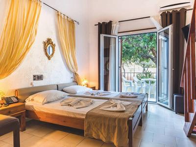 Bright hotel room with double bed, golden curtains, and balcony access overlooking garden.