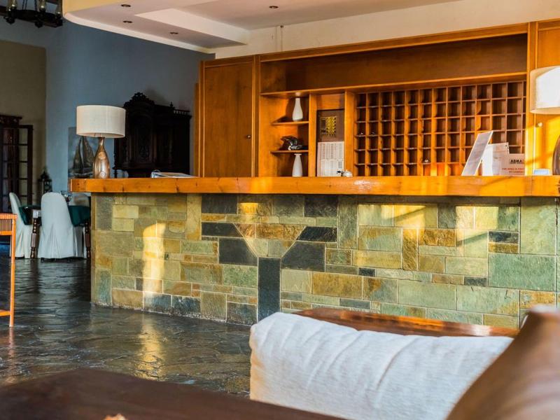 Hotel reception with stone counter, chairs, and illuminated shelving area behind.