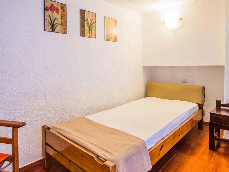 Small simple bedroom with a single bed, wooden furniture, and flower paintings on the wall.