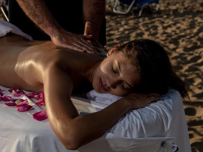 Žena dostává relaxační masáž venku na lehátku s květinovými okvětními lístky.