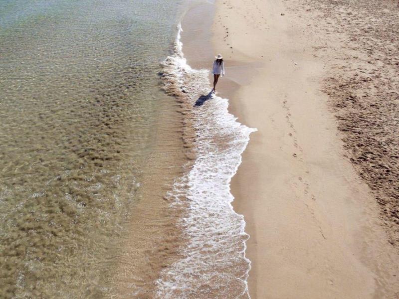 Osoba stojí na okraji vody na široké, písečné pláži.
