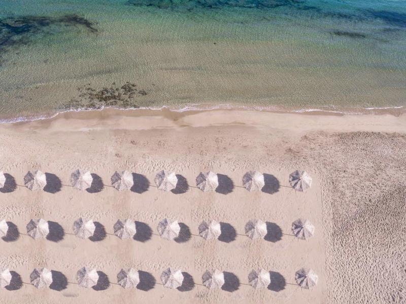 Letecký pohled na pláž s rovnoměrně rozmístěnými slunečníky a čistou mořskou vodou.