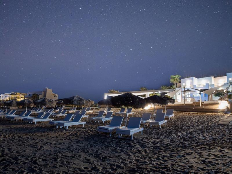 Prázdná pláž s lehátky před osvětleným hotelem pod jasnou hvězdnou noční oblohou