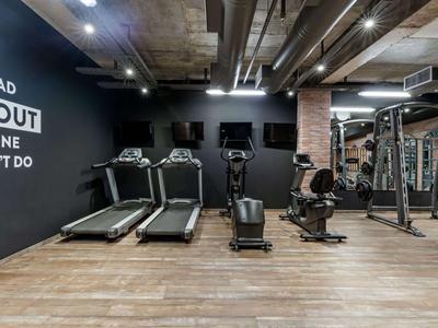 Palestra moderna con tapis roulant, vogatori e area per allenamento di forza su pavimento in legno.