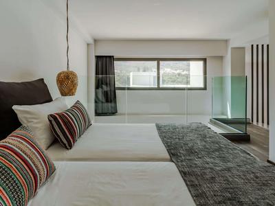 Moderní hotelový pokoj se dvěma postelemi, velkými okny a minimalistickým designem.