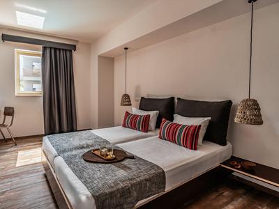 Moderní hotelový pokoj s manželskou postelí, dekorativními polštáři, psacím stolem a oknem s závěsem.