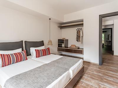 Moderní hotelový pokoj se dvěma jednolůžky, šedými polštáři a dřevěnou podlahou.