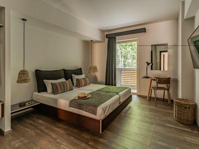 Camera d'hotel moderna con letto matrimoniale, scrivania, TV e vista sul balcone con piante verdi.