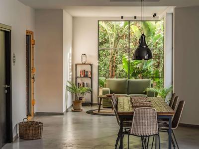 Area pranzo moderna con tavolo in legno e panca verde davanti a una grande finestra che dà sul verde.