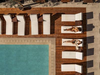 Vista drone di una piscina con lettini bianchi e due bagnanti.