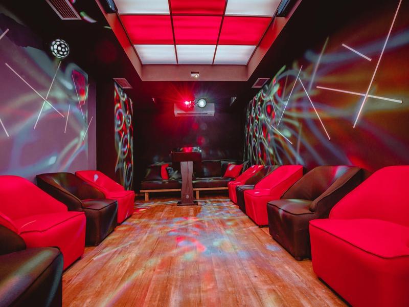 Živý salonek s červenými a hnědými sedadly, dřevěnou podlahou a barevným osvětlením stropu.