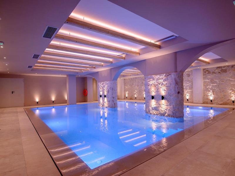 Vnitřní bazén s modrou vodou a elegantním stropním osvětlením v hotelu.