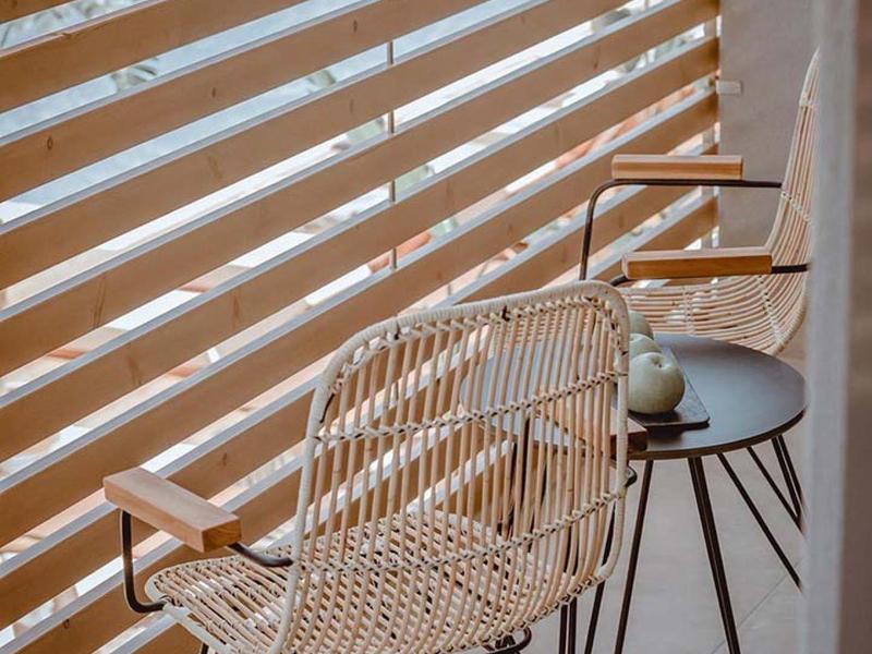 Balkon s dvěma pletenými židlemi a malým kulatým stolem s výhledem na bazén.