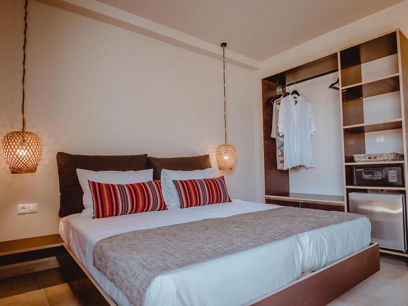 Moderní ložnice s velkou postelí, závěsnými lampami a otevřenou skříní s oděvy a trezorem.