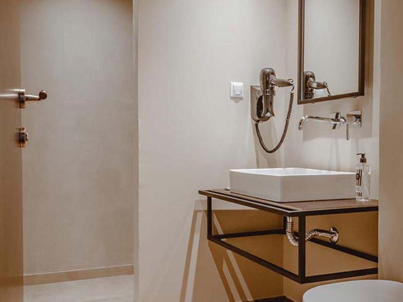 Moderní hotelová koupelna s dřevěnou podlahou, bílými stěnami, skleněnou sprchou a elegantním černým rámem zrcadla.