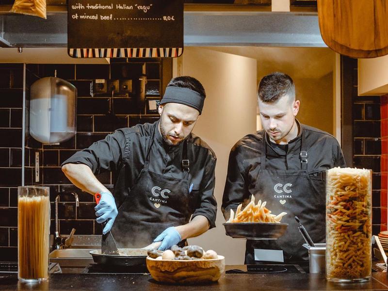 Dva kuchaři vaří v restauraci s kořením a sklenicemi těstovin.
