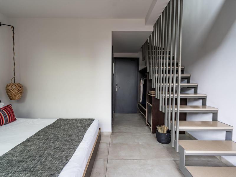 Moderní hotelový pokoj s manželskou postelí a otevřeným schodištěm na zdi.