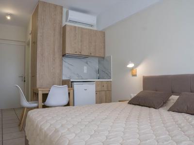 Malý hotelový pokoj s postelí, stolem, židlí, mini lednicí a klimatizací.