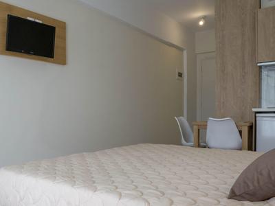 Jednoduchý hotelový pokoj s postelí, židlemi, stolem a televizí na stěně.