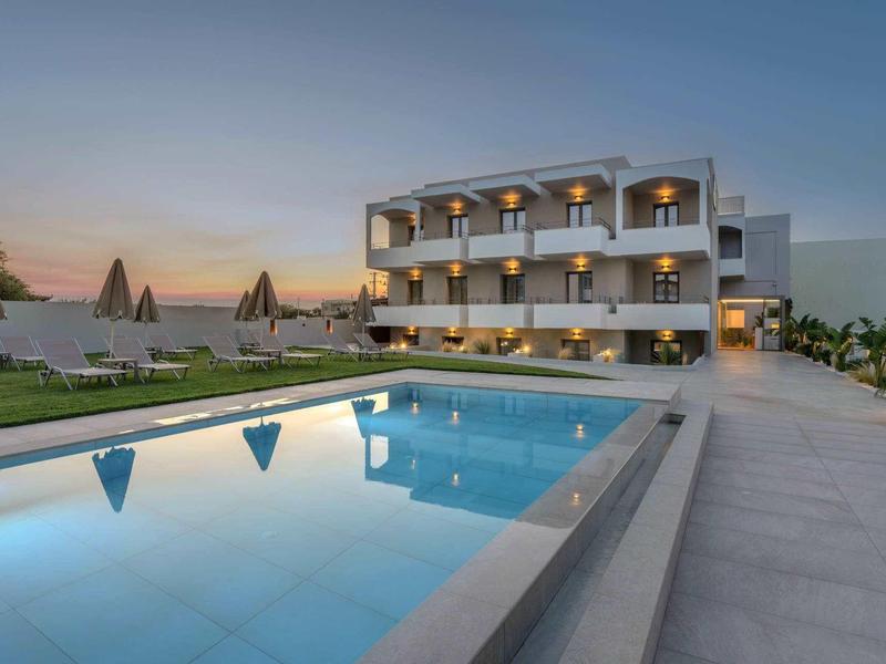 Moderní hotelový komplex s bazénem při západu slunce a lehátky na terase.