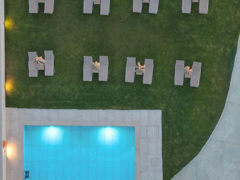 Pohled shora na obdélníkový bazén a lehátka na trávnících.