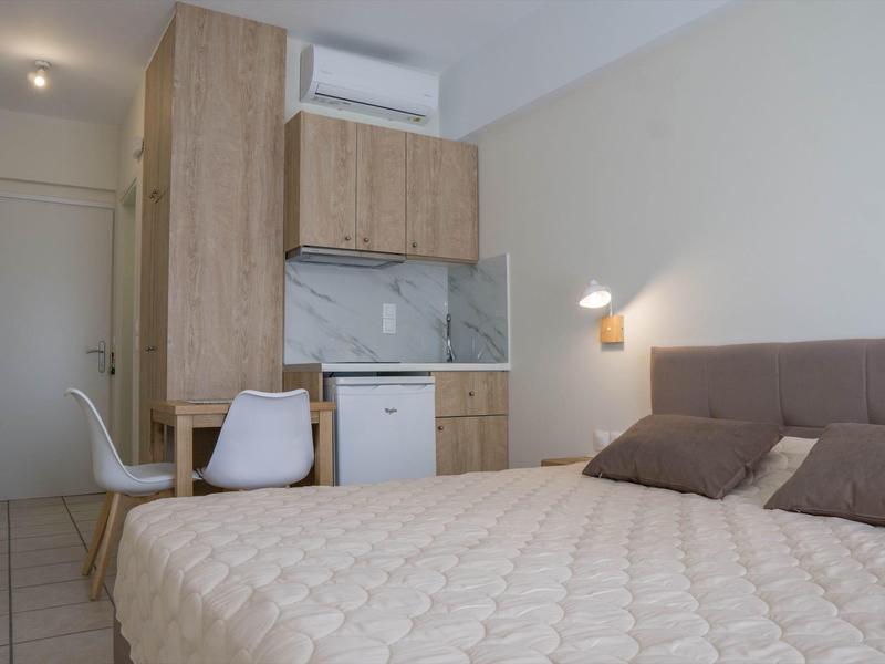 Malý hotelový pokoj s postelí, stolem, židlí, mini lednicí a klimatizací.