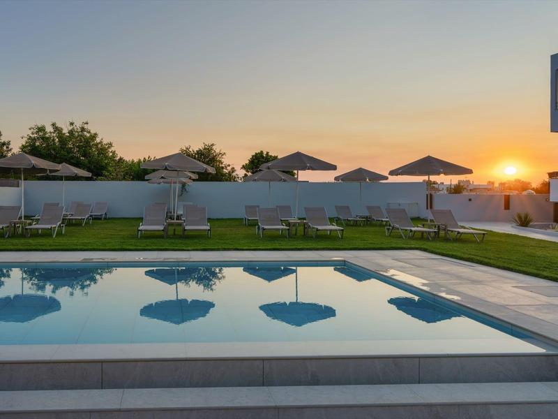 Západ slunce nad bazénem s deštníky a lehátky vedle hotelu.