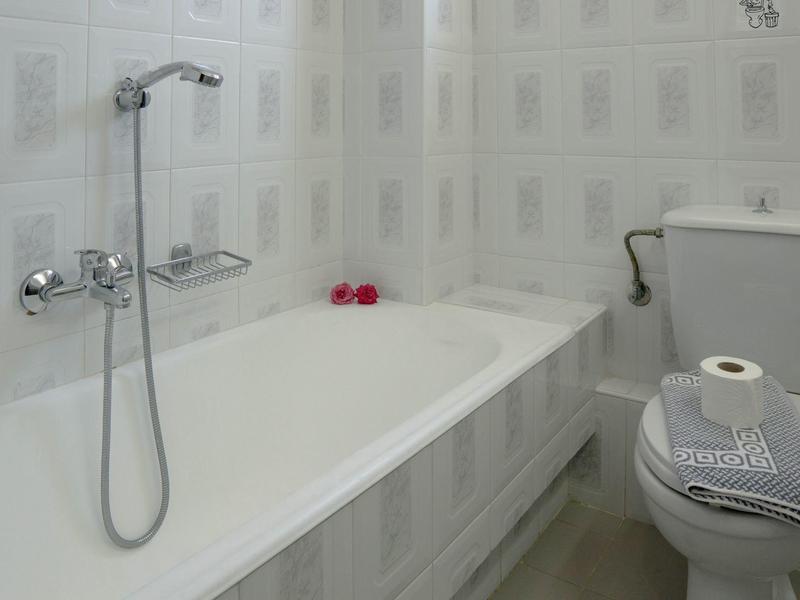 Malá koupelna s vanou, sprchovou hlavicí, toaletou a toaletním papírem.