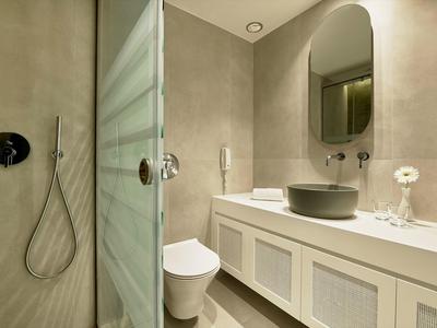 Modernes Badezimmer mit grauen Fliesen, freistehender Dusche, Weißem WC und großem Waschtisch.