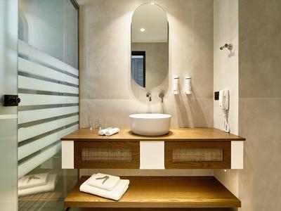 Nowoczesna łazienka z okrągłym lustrem, umywalką na drewnianej szafce i ręcznikami.